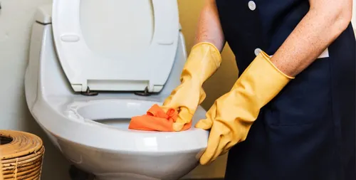 Maintenance worker wearing gloves cleaning a toilet, a required task on an apartment turnover checklist.